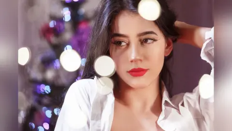JessieLiu poses with one hand behind her head, wearing an open white button-down shirt against a soft, dark background.