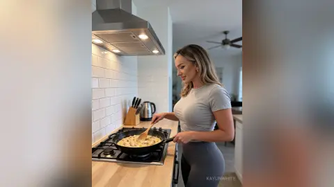 Blonde woman in grey casual outfit cooking food in a modern kitchen with white subway tile backsplash.