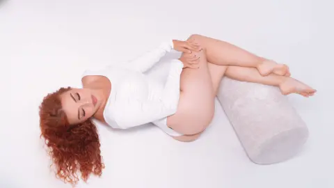 Redheaded woman in a white long-sleeve top relaxing on a white floor in a bright, minimalist studio setting.