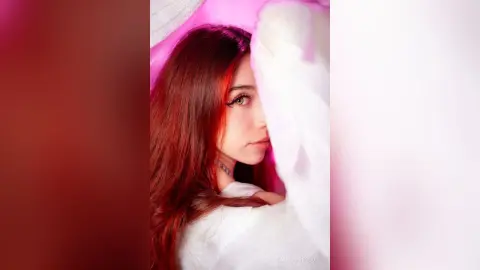 Young woman with long brown hair peeking through soft white fabric in a dreamy pink aesthetic setting.