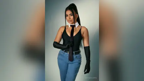 Stylish woman in a black bodysuit, necktie, and long gloves posing confidently against a grey studio background.