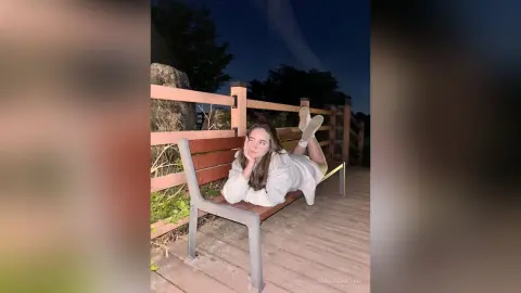 Young woman in white loungewear relaxing on a wooden deck under a night sky.