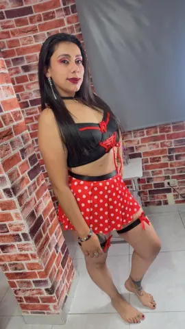 Woman in red polka dot crop top and mini skirt posing against a brick wall in a studio setting.