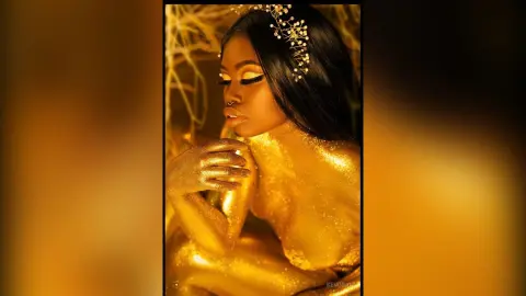 KeianHoz poses with gold glitter covering her skin and chest, wearing a decorative gold headpiece.