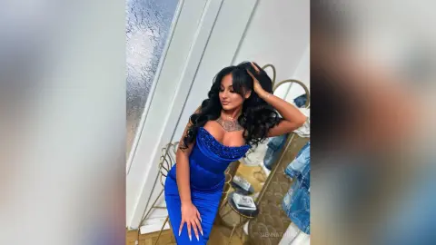 Glamorous woman in a sparkling royal blue evening gown posing in a bright room.