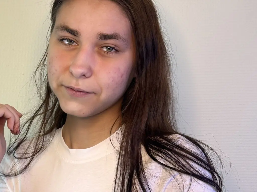 AngelaDefelice poses with long brown hair and a white t-shirt against a plain white wall.