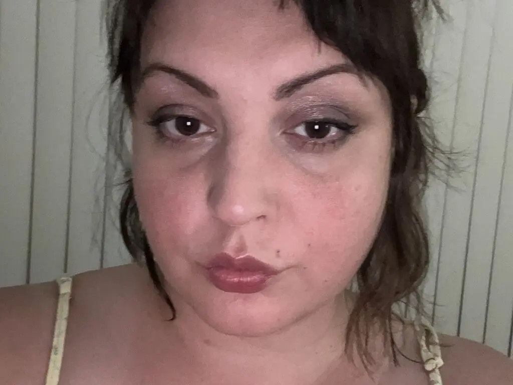 Close-up portrait of a woman with dark hair and smoky eye makeup posing in a casual indoor setting.