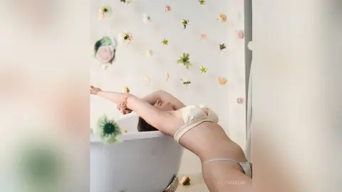 Relaxed woman in white bikini relaxing in a bathtub against a floral wall background.