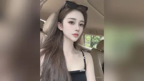 AgelaHui poses in a car wearing a black tank top, looking at the camera with long brown hair and sunglasses on her head.