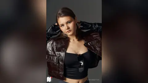 CaritaMattox poses in a dark leather jacket and black tank top with her hands behind her head.