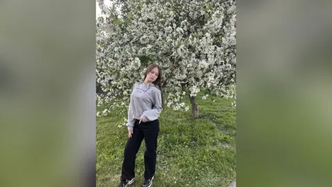 Young woman in a grey sweatshirt and black pants posing in a blooming white flower garden during spring.