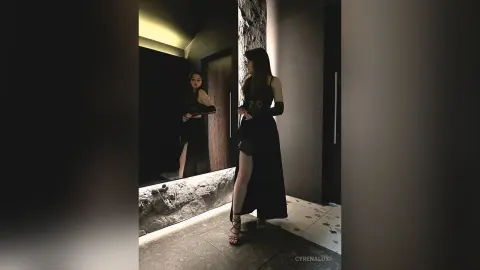 Elegant woman in a black evening gown standing in a moody, dimly lit luxury modern interior.