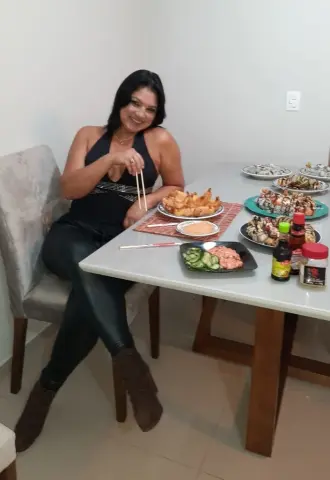 Smiling woman in a black tank top enjoying sushi and fried appetizers at a dining table.