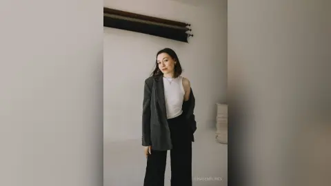 Elegant woman in a white tank top and grey blazer posing in a minimalist, bright modern room.