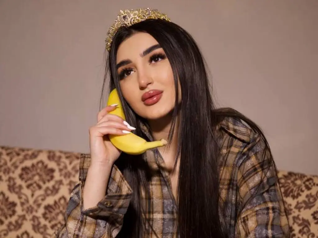 JuliDeming wears a gold tiara and a plaid shirt while holding a yellow banana against her cheek.