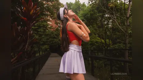 Young woman in a red crop top and white mini skirt posing in a lush green garden setting.
