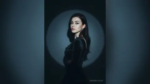 Elegant woman in a black velvet dress posing against a dramatic spotlight in a moody studio setting.