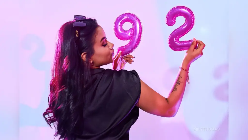 MilyThomas β Young woman in a black top celebrating a 92nd birthday with pink foil balloons in a bright studio setting.