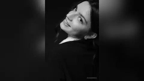 Smiling young woman in a black outfit posing for a moody black and white portrait.