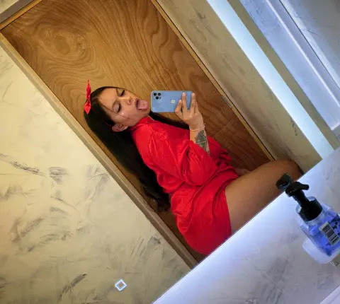 Young woman in a red satin robe taking a playful mirror selfie in a modern bathroom.