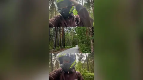 Motorcyclist in a brown jacket and black helmet riding through a lush green forest on a paved road.