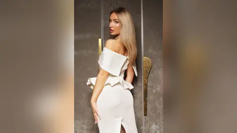 Elegant blonde woman in a white off-the-shoulder cocktail dress posing in a modern interior setting.