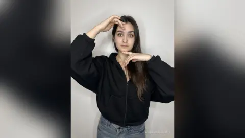 Young woman in a black zip-up hoodie posing against a plain white background with a calm expression.