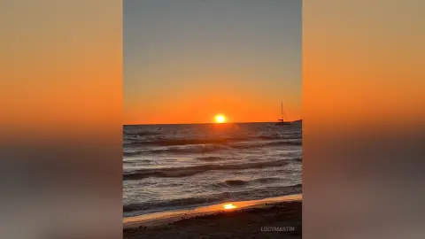LucyMartin watches the sunset over the ocean waves on a sandy beach.
