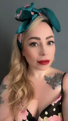 FrankiiRayeXXXX poses with blonde wavy hair and a teal headwrap, wearing a black floral print camisole that shows her chest and shoulder tattoos.