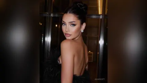 Glamorous woman in a black feathered evening gown posing elegantly in a luxury indoor setting.