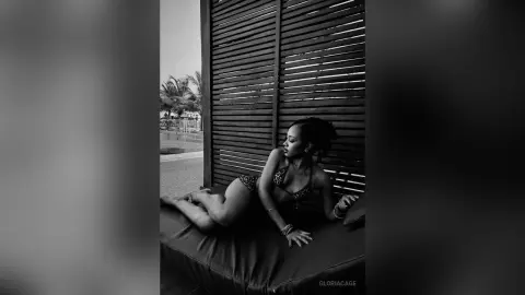Elegant woman in a patterned bikini relaxing on a lounge chair against a wooden slatted wall in black and white.