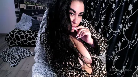 Woman with long dark hair wearing a leopard print faux fur coat in a cozy indoor setting.