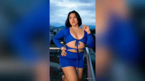 KimRoberth poses on a balcony wearing a blue long-sleeved cutout bodysuit with a tie-front detail.