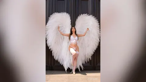 Woman in white lace lingerie and large feathered angel wings posing against a dark door.