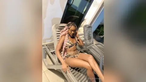 Smiling Black woman in a leopard print bikini relaxing on a lounge chair by a sunny outdoor patio.