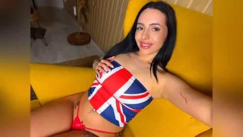 Smiling woman in a Union Jack tube top relaxing on a bright yellow sofa in a cozy room.
