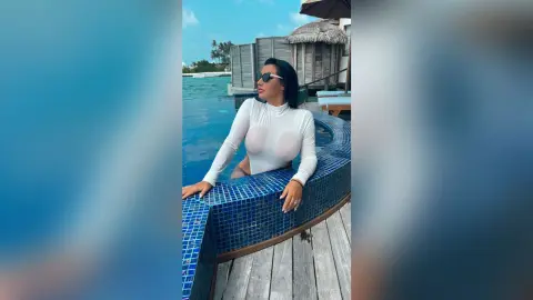 MissyJolie wears a white long-sleeve bodysuit while sitting on the edge of a blue tiled swimming pool.