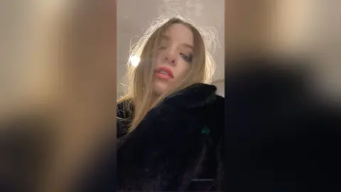 Blonde woman in a cozy black faux fur coat posing with a moody, cinematic aesthetic indoors.