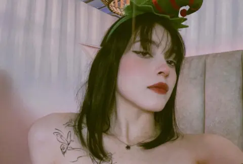 Young woman with elf ears and dark hair posing in a festive holiday costume with a soft, dreamy mood.
