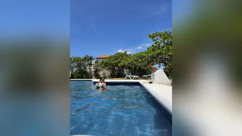 Young woman in a blue bikini relaxing in a luxury resort swimming pool under a clear sunny sky.