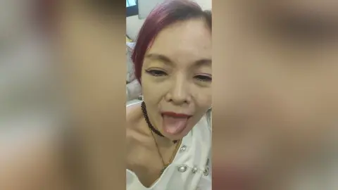 OishiMeily — Smiling woman with red hair in a white sleeveless top making a playful expression indoors.