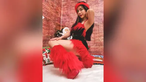 JessieLiu poses in a black and red furry outfit with red hair accessories against a brick wall background.