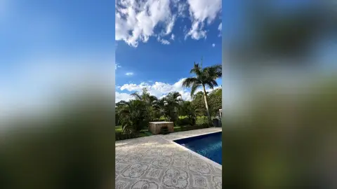 Tropical backyard oasis featuring a luxury swimming pool and patterned stone patio under a bright blue sky.
