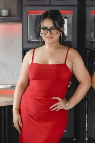 Smiling woman in a red satin slip dress and glasses posing in a modern kitchen setting.