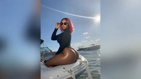Stylish woman in a black bodysuit and sunglasses relaxing on an inflatable raft in the ocean under a sunny sky.