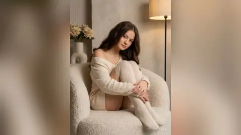 Young woman in a cozy cream knit sweater and thigh-high socks sitting in a warm, minimalist living room.