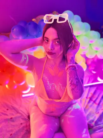 maaeve_elf — Woman in yellow bikini with neon body paint posing amidst colorful glowing balloons in vibrant pink lighting.