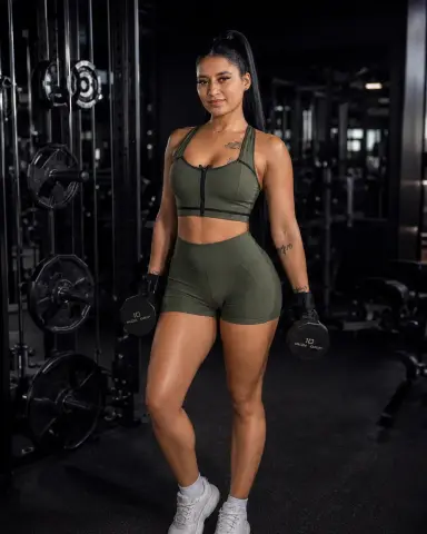 Fit woman in olive green gym set holding dumbbells in a modern fitness center.