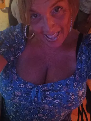 BBWgoDDDess — BBWgoDDDess smiles while wearing a blue floral print top that shows off her cleavage and large breasts.