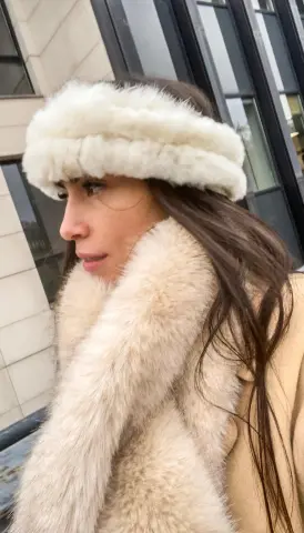 Woman in cozy white faux fur headband and fluffy winter scarf posing outdoors in stylish cold weather fashion.